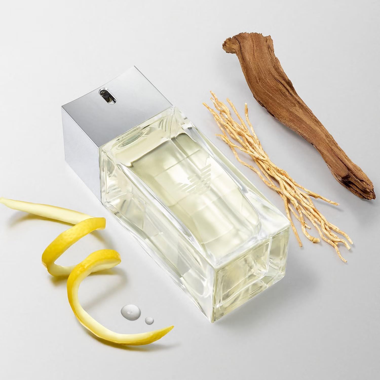 Flacone di Emporio Armani Diamonds for Men con note. Flacone accanto a scorza di limone, legno ed erbe.