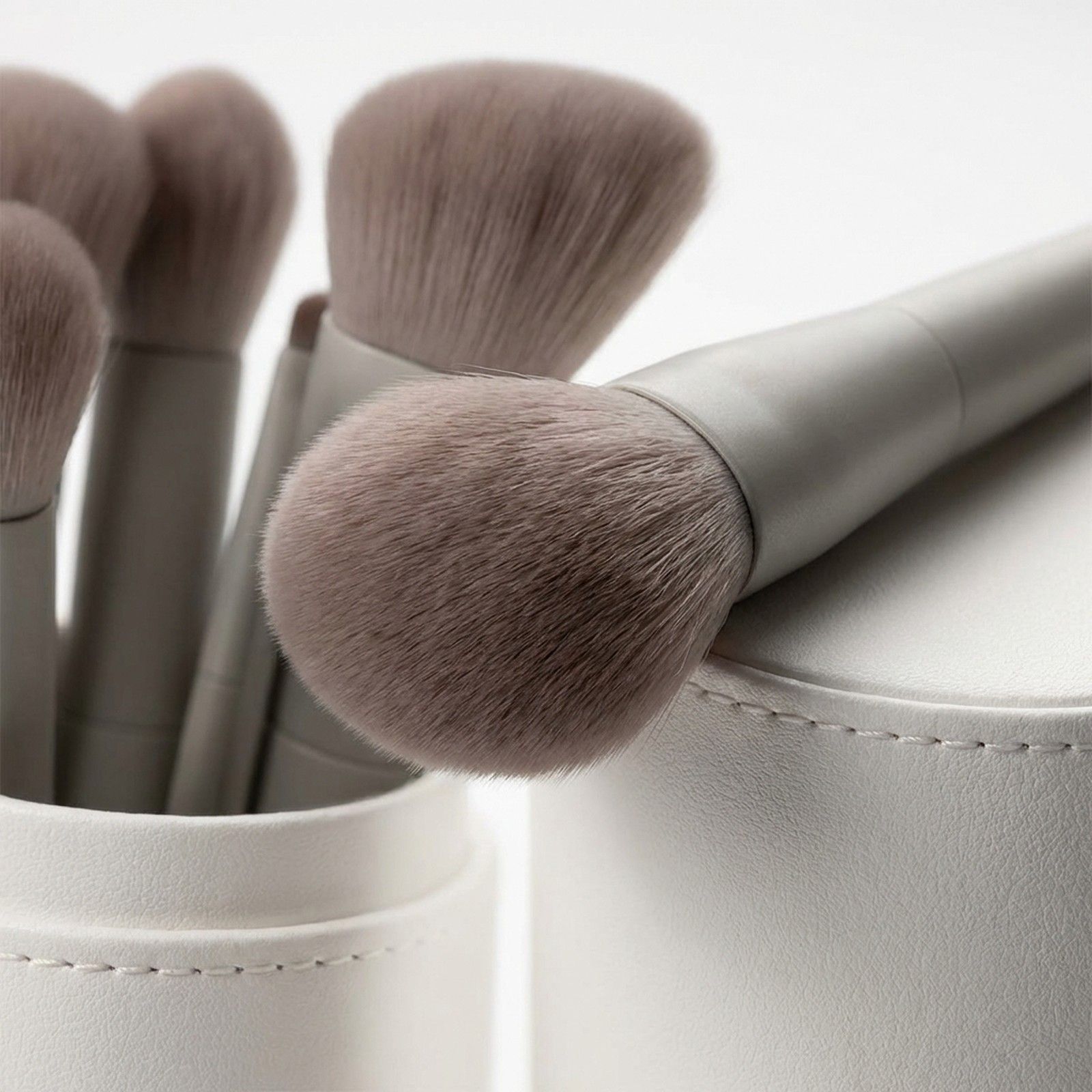 Set di pennelli da trucco grigi con setole morbide in un portaoggetti bianco.