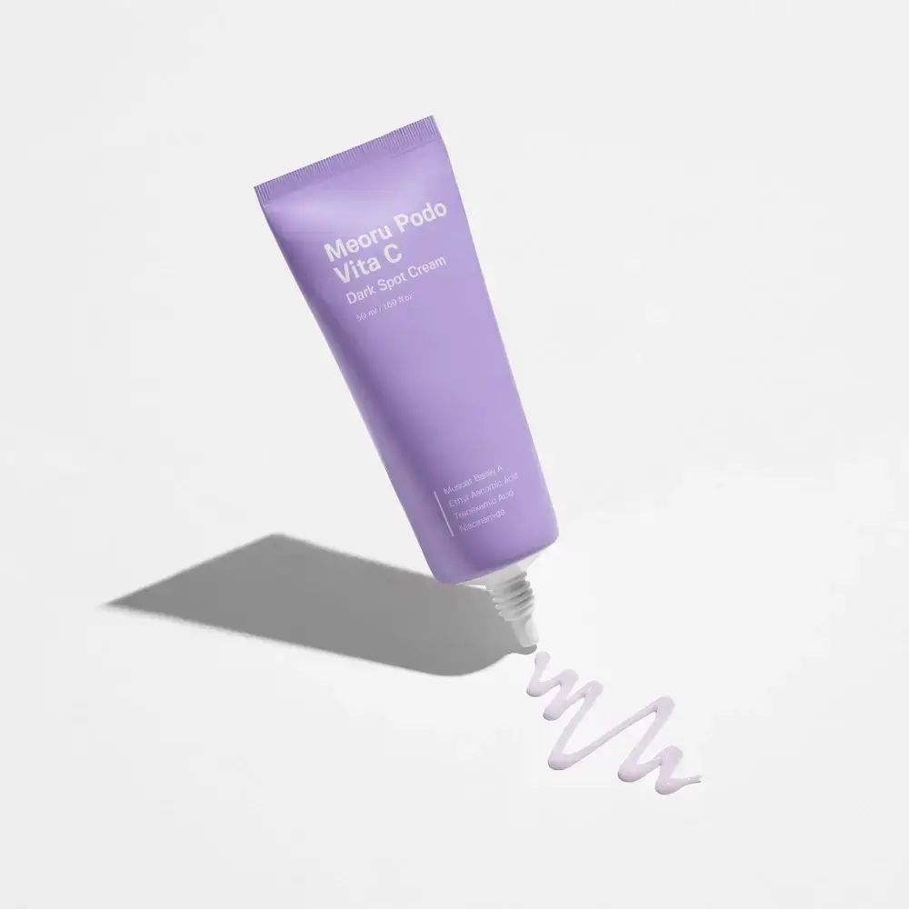 Tubo viola 'Meoru Podo Vita C Dark Spot Cream'. Crema che esce dal tubo. Sfondo bianco.