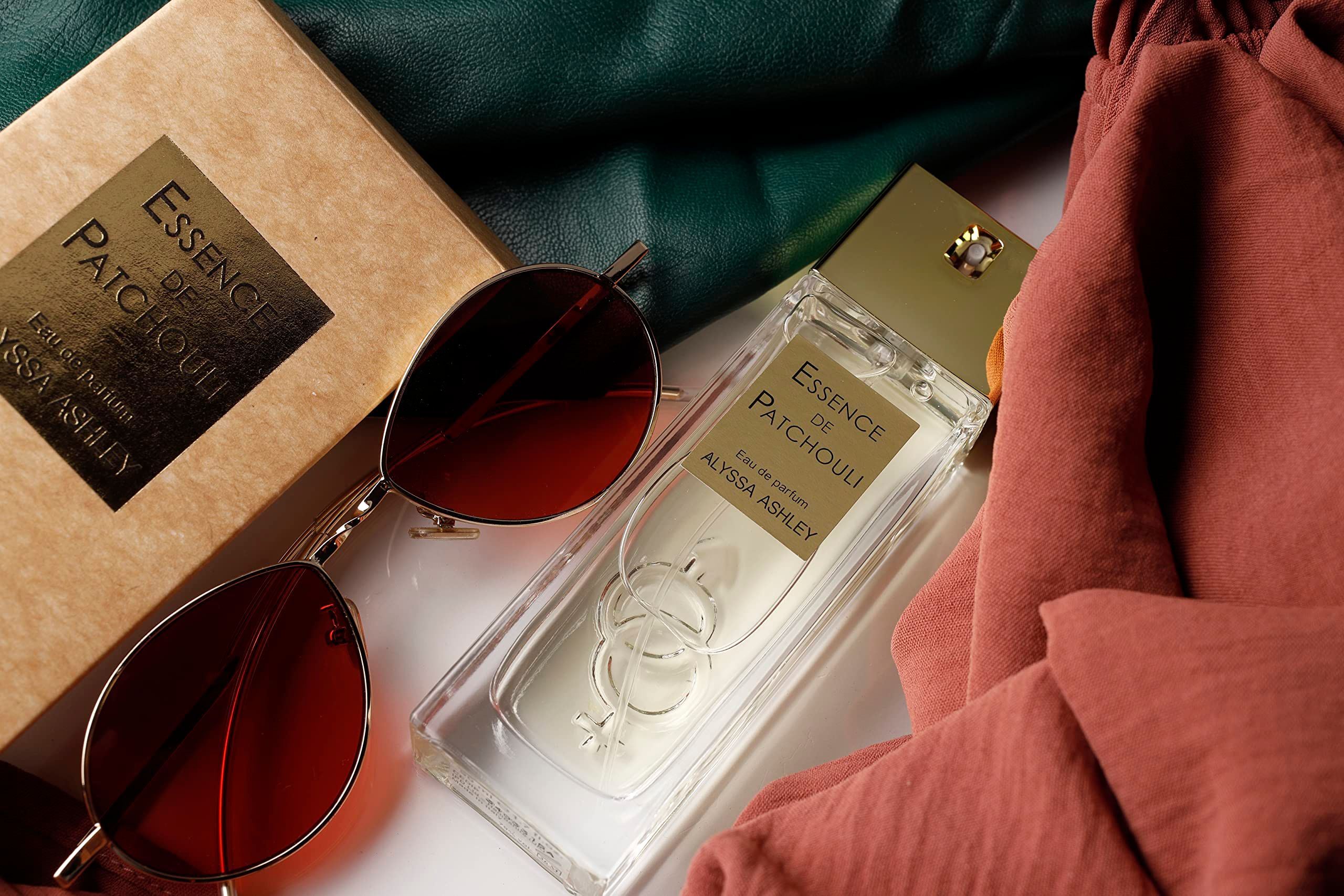 Flacone Alyssa Ashley Essence de Patchouli Eau de Parfum, occhiali da sole e tessuto.