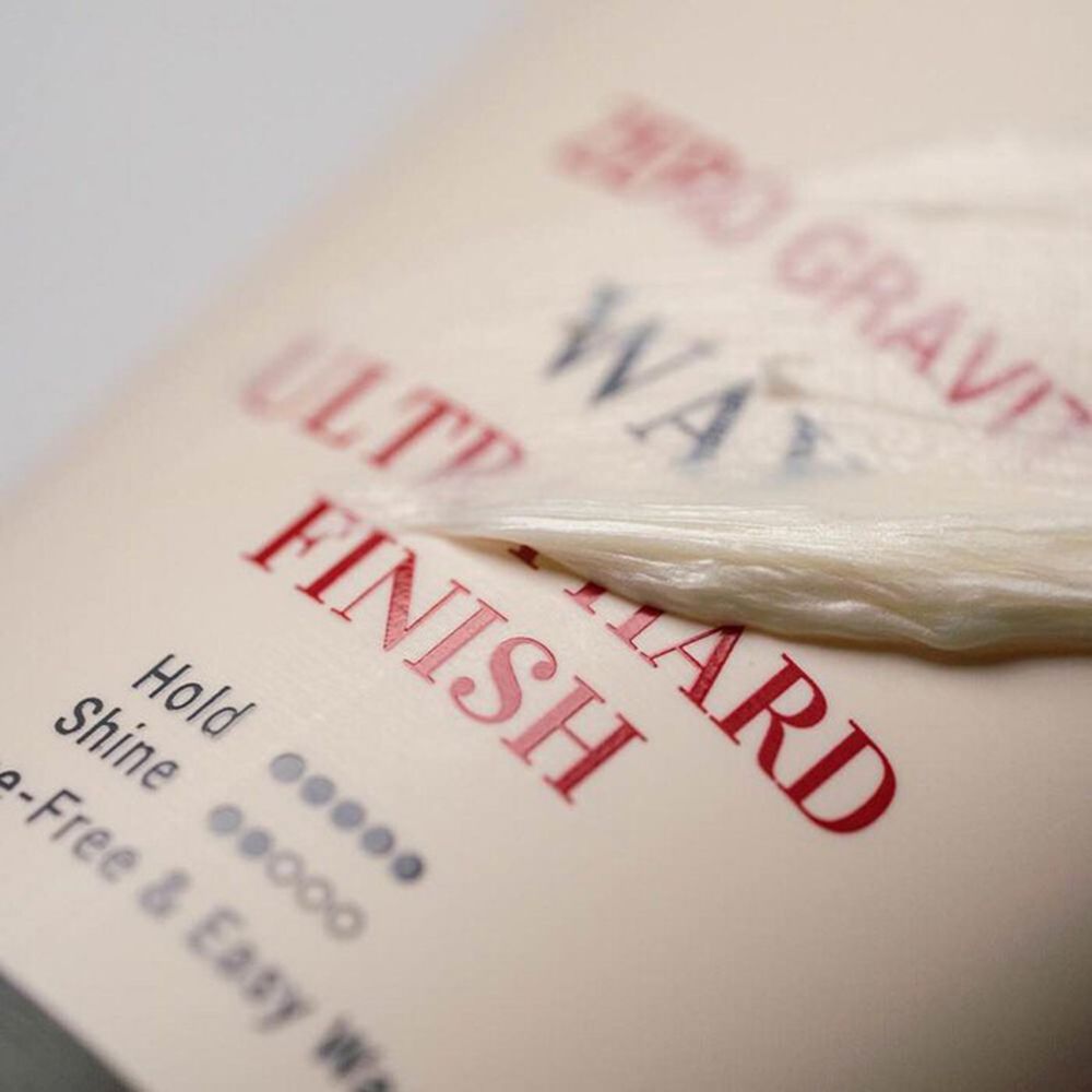 Primo piano della scritta del prodotto: Zero Gravity Wax, Ultra Hard Finish. Scritta rossa e blu su sfondo beige.