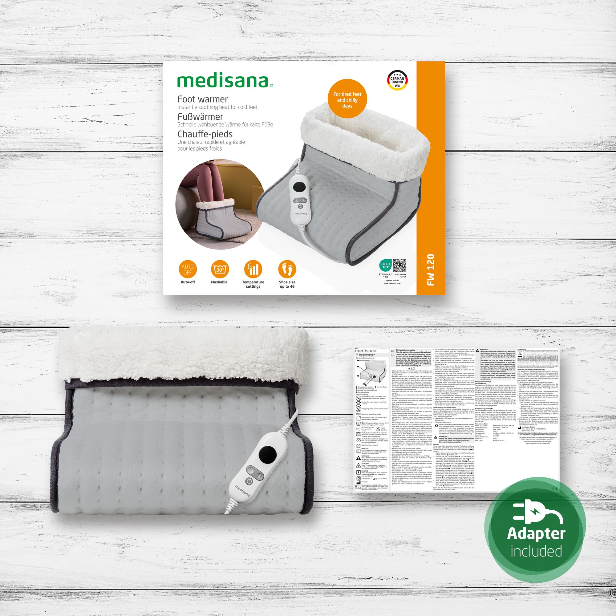 Confezione del prodotto con scaldapiedi, pannello di controllo e accessori. Testo: Adattatore incluso, FW 120. Il prodotto è grigio con fodera interna bianca.