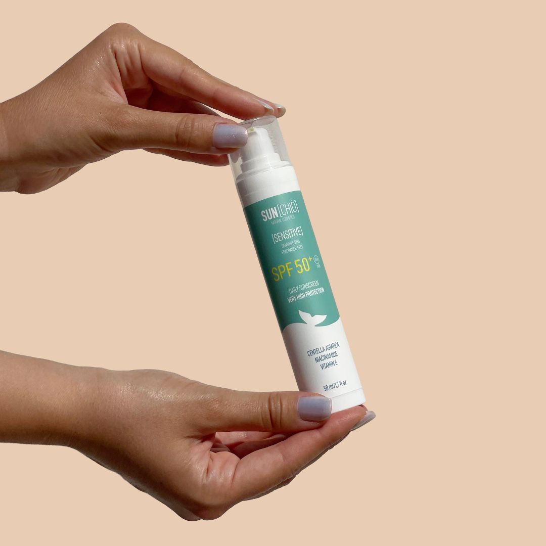 Mani che tengono un flacone di crema solare SPF 50+ con scritta 'SENSITIVE'.