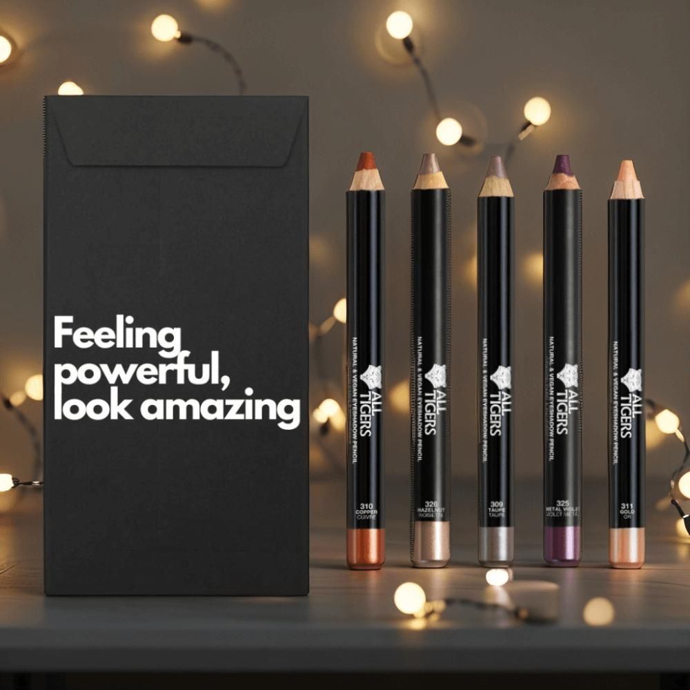 Cinque matite occhi accanto a busta nera con testo. Matite di diversi colori, con logo e nome del prodotto.