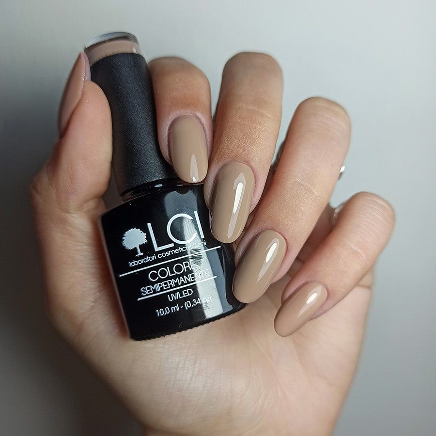 Mano con flacone di smalto e unghie smaltate. Flacone con smalto marrone. Unghie colorate di marrone.