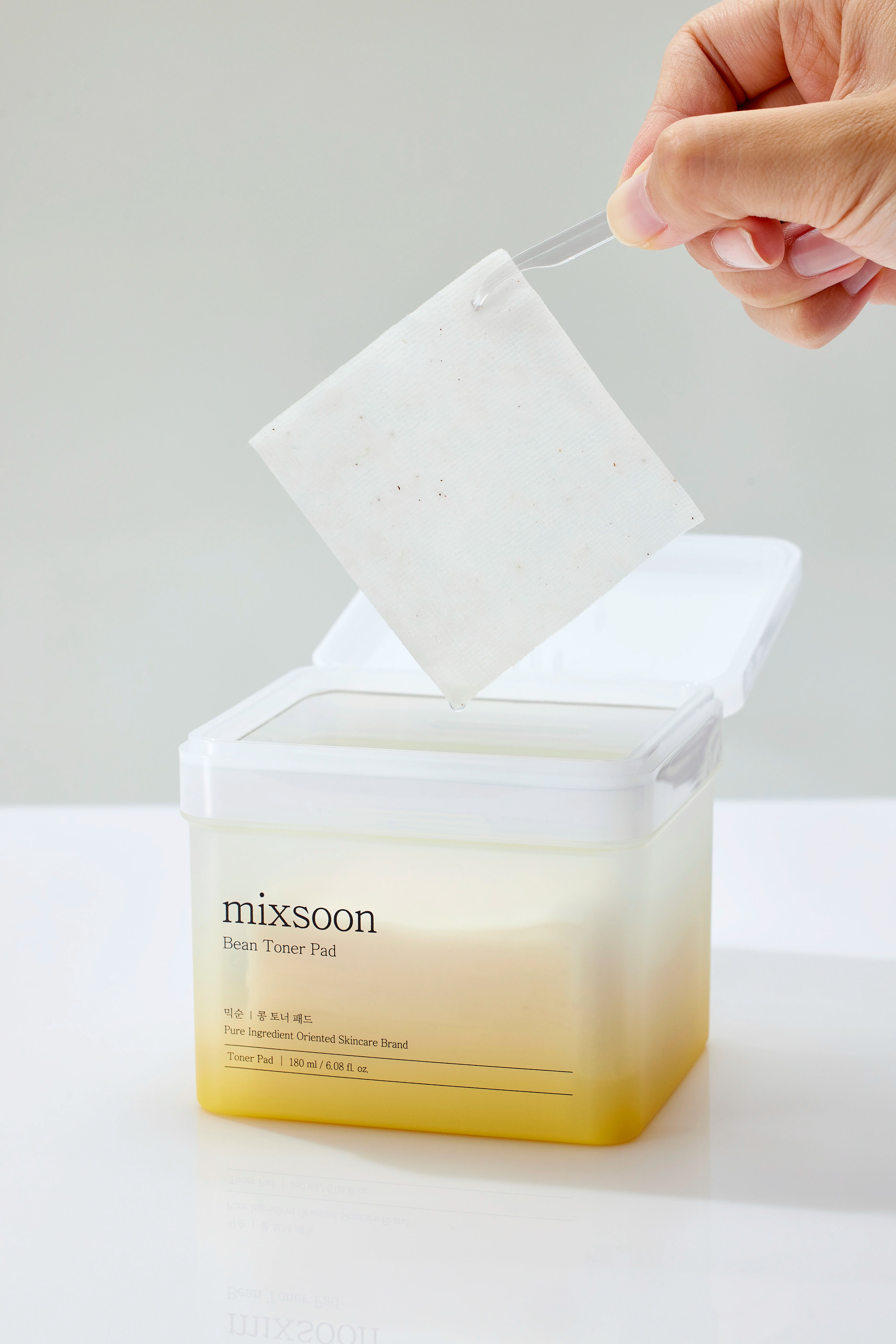 Contenitore "mixsoon Bean Toner Pad" aperto. Mano che preleva un pad. Nome e dettagli del prodotto visibili.
