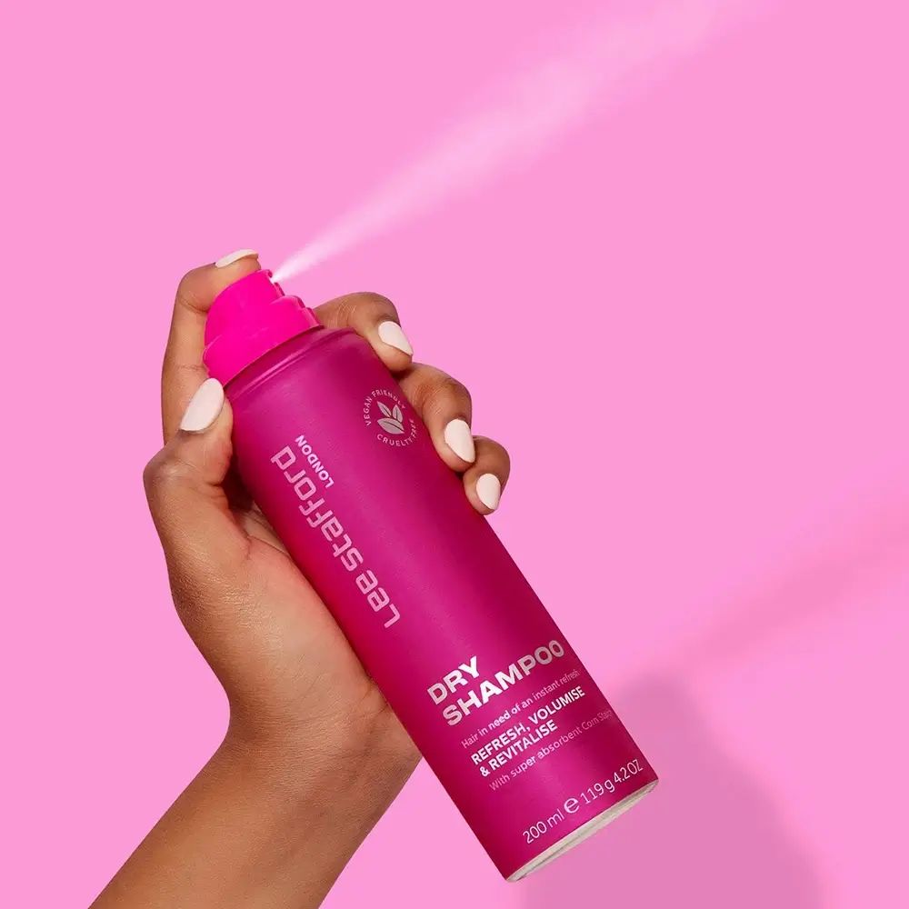 Mano che tiene una bomboletta di shampoo secco rosa. Nebbia spray. Scritta: LEE STAFFORD LONDON, DRY SHAMPOO, REFRESH, VOLUMISE & REVITALISE.