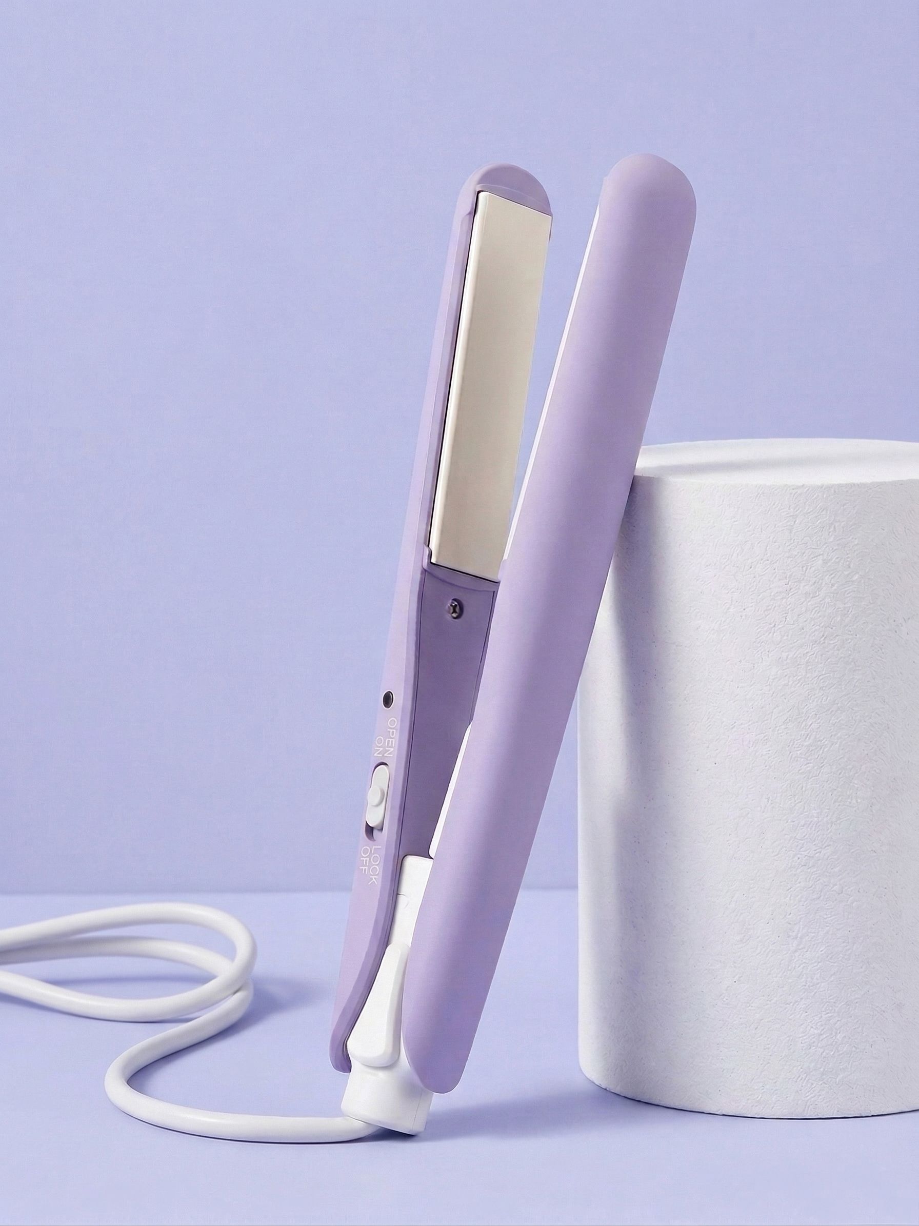 Piastra per capelli viola con cavo bianco, in piedi accanto a un cilindro bianco.