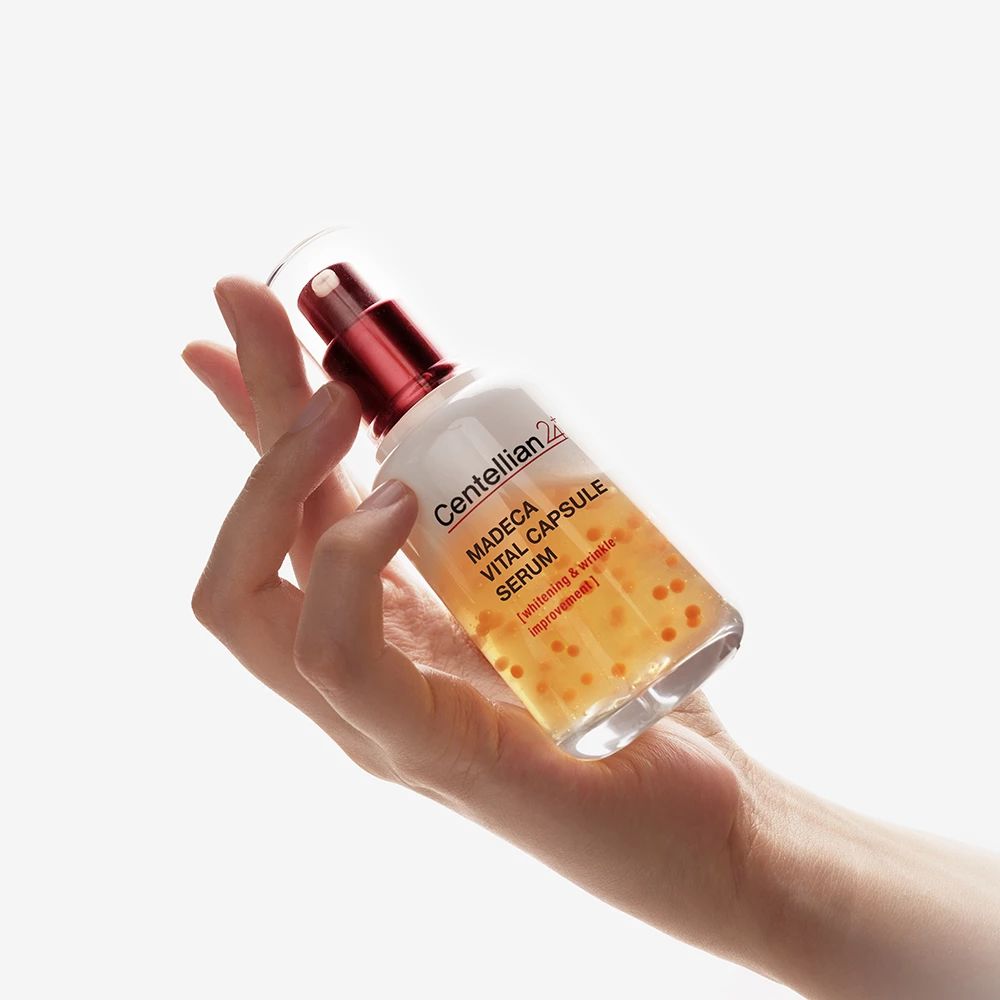 Mano che tiene il flacone di siero. Nome del prodotto e marchio visibili. Flacone con dettagli rossi.