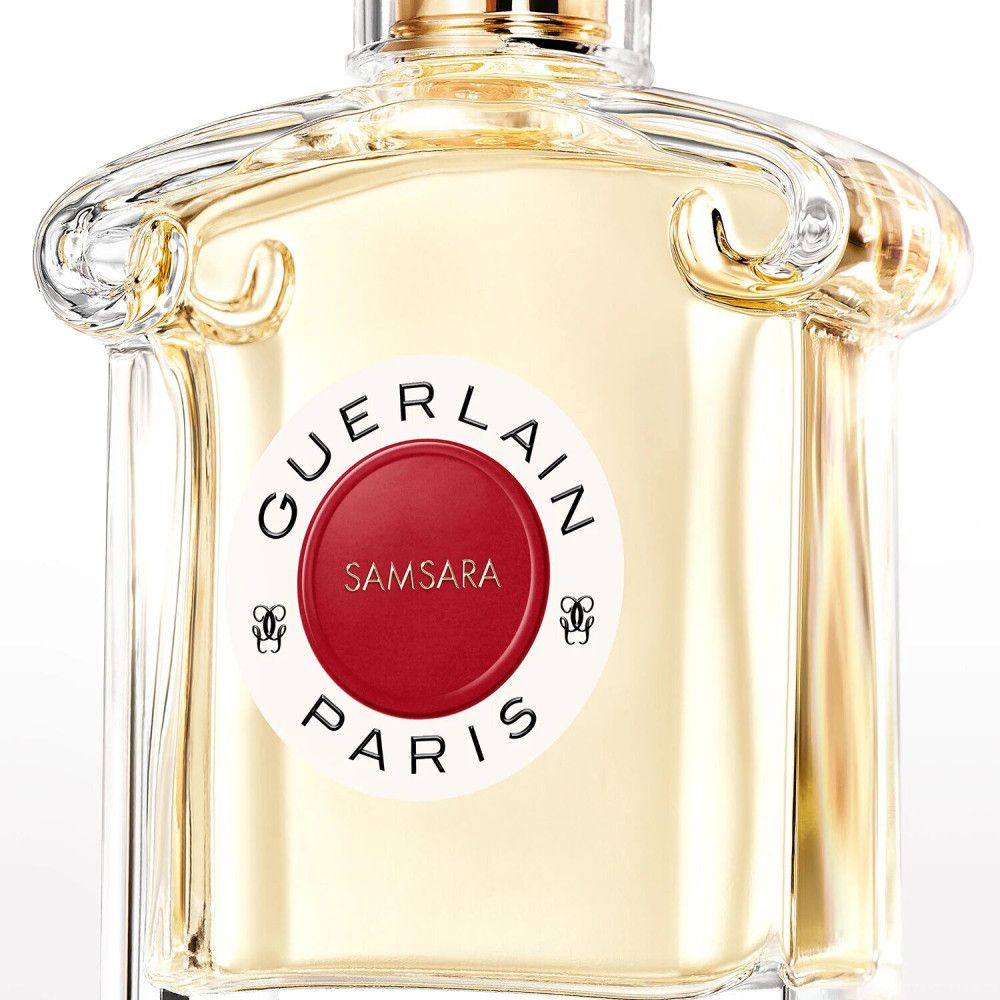 Flacone di profumo con etichetta rossa. Scritta: GUERLAIN PARIS, SAMSARA. Flacone in vetro trasparente con tappo dorato.