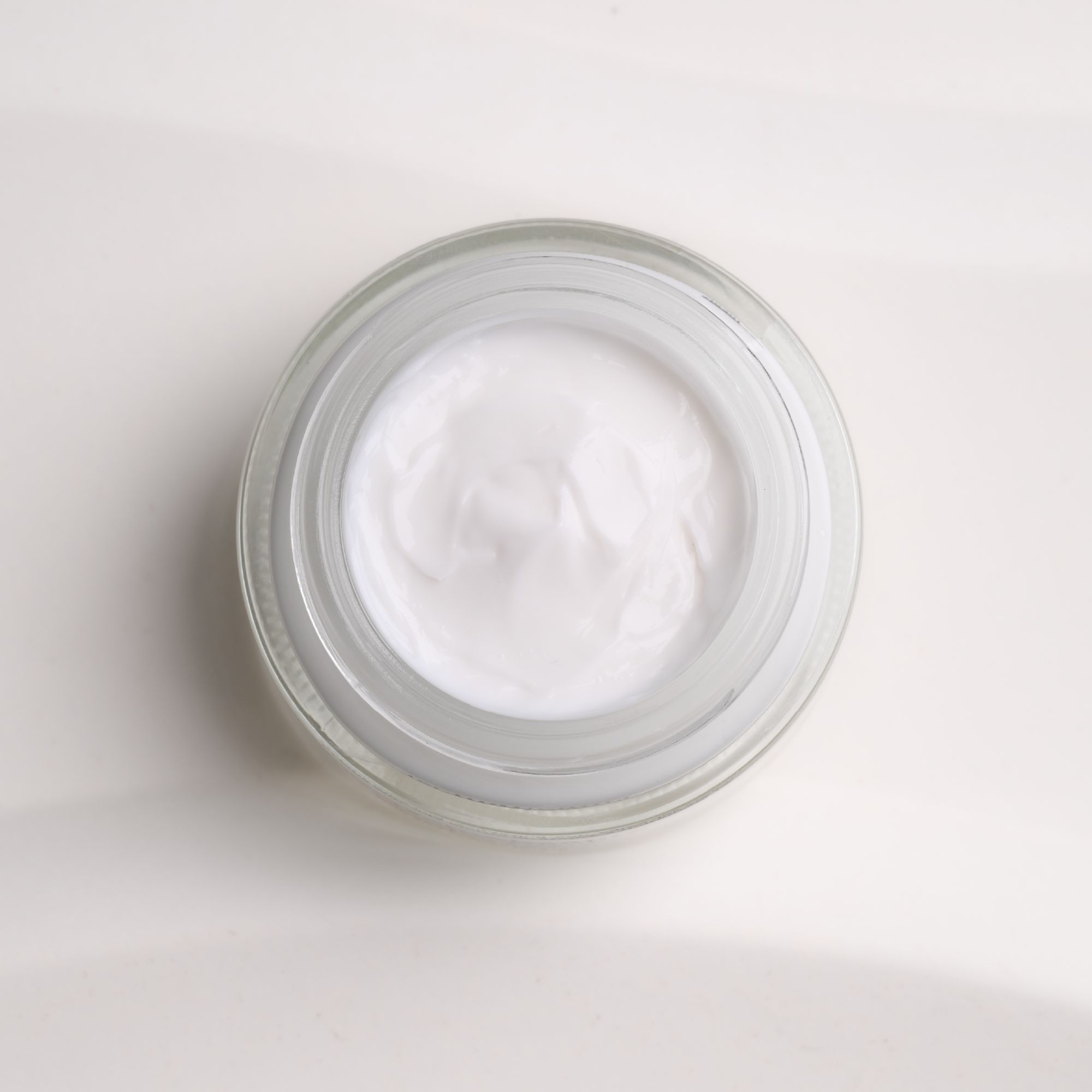 Vaso di vetro aperto con crema bianca. Vista dall'alto. Superficie strutturata. Senza coperchio.