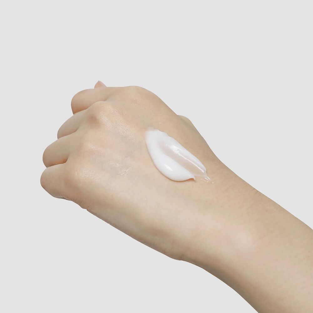 Mano con crema bianca. Applicazione di crema sul palmo. Colore della pelle chiaro. Lo sfondo è grigio chiaro.