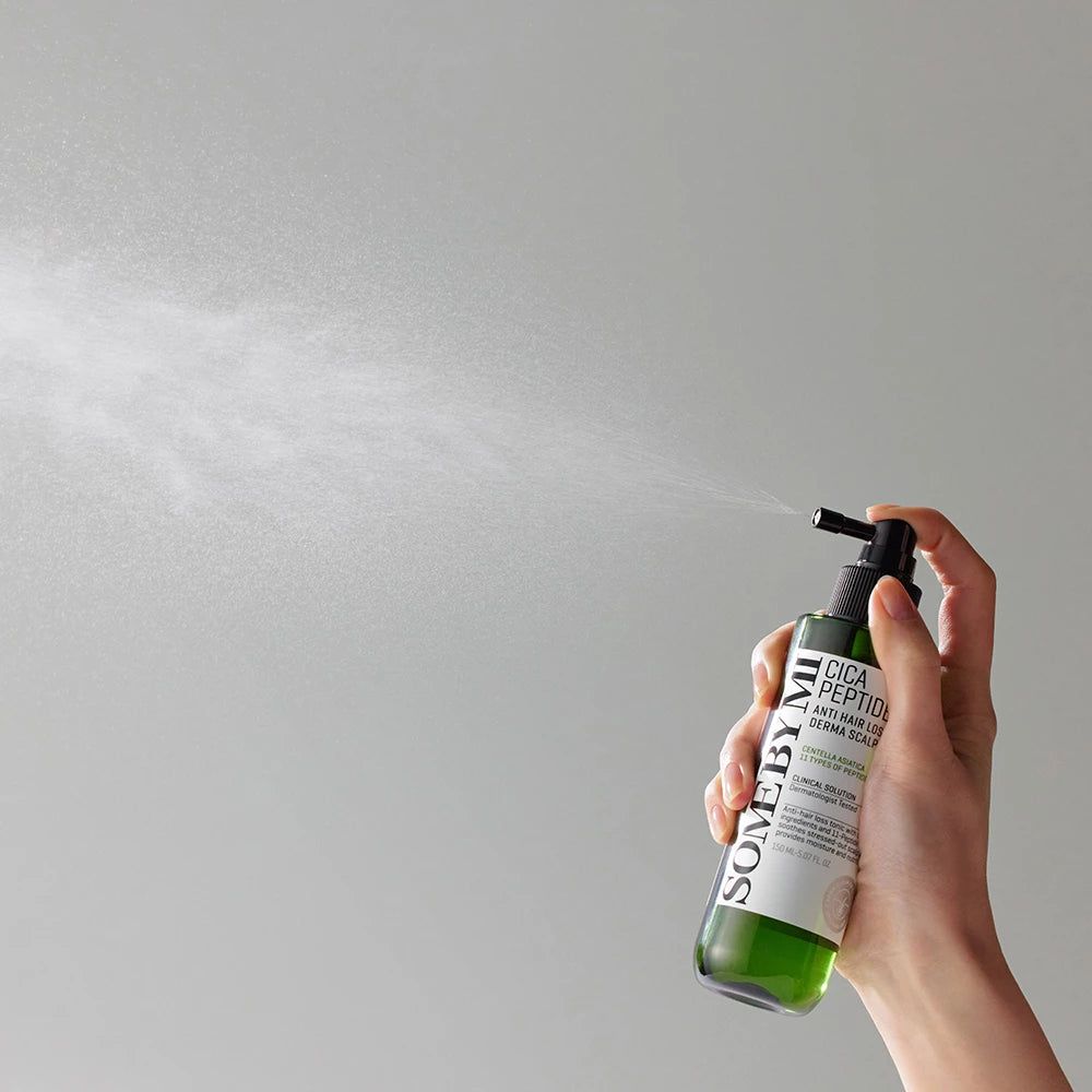 Mano tiene in mano un flacone verde con erogatore nero. Scritta: Cica Peptide Anti Hair Loss Derma Scalp Tonic. Marchio: SOME BY MI. Nebbia.
