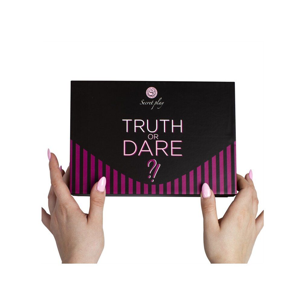 Mani che tengono una scatola del gioco "Truth or Dare". Scatola nera con strisce rosa e scritta. Unghie rosa.