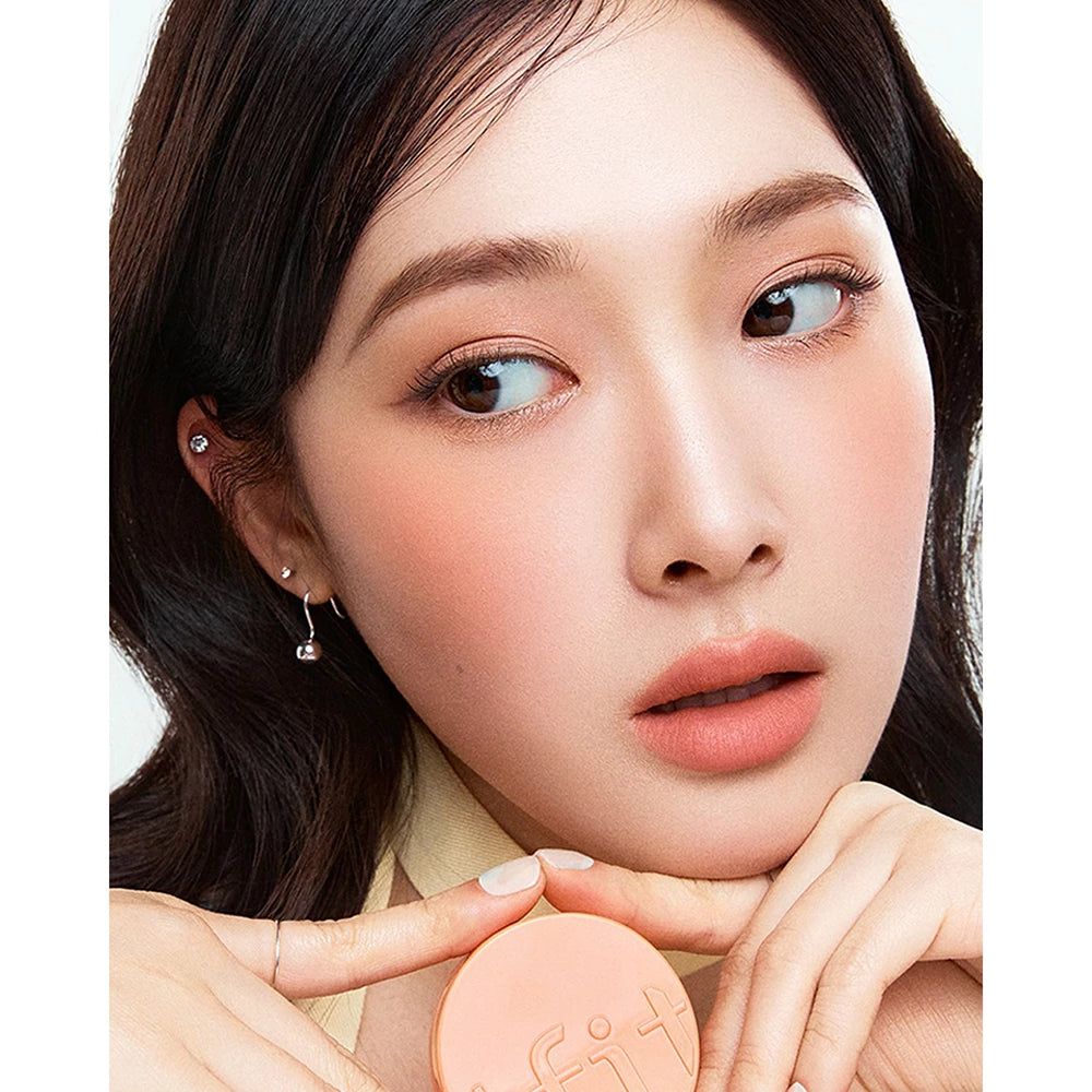 Una donna tiene in mano un blush TFIT Fluffy Velvet Cushion Blush color pesca. Il prodotto è applicato sulle sue guance.