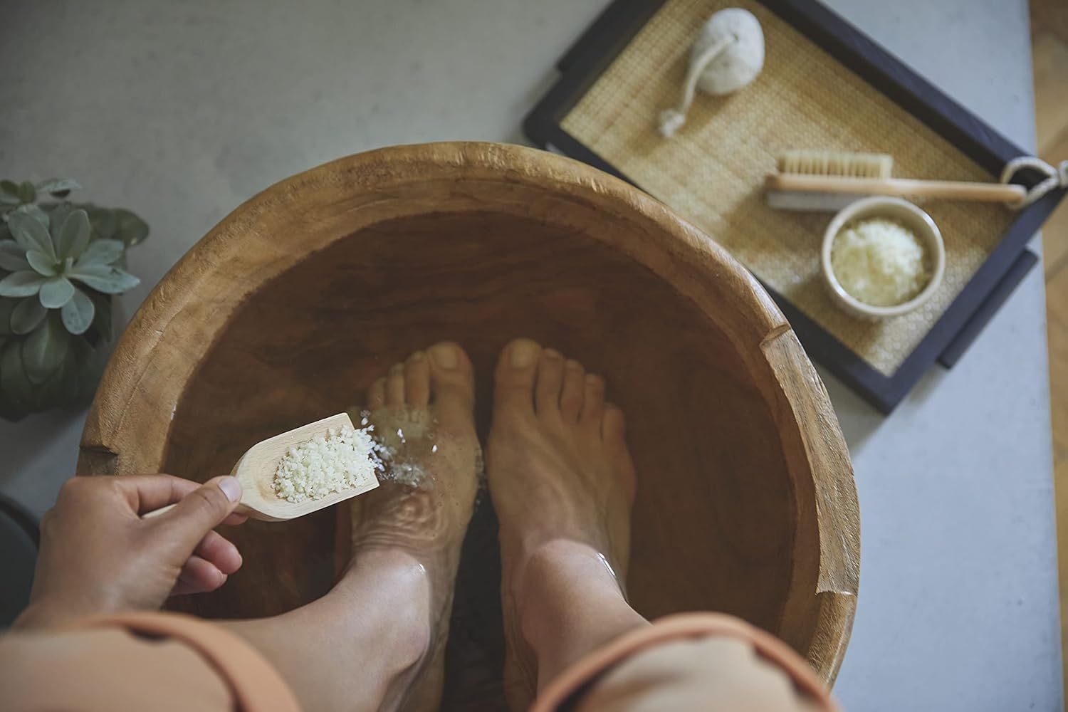 Piedi in una bacinella di legno con acqua. Persona versa cristalli sui piedi con un cucchiaio. Accessori: spazzola, spugna, vassoio.