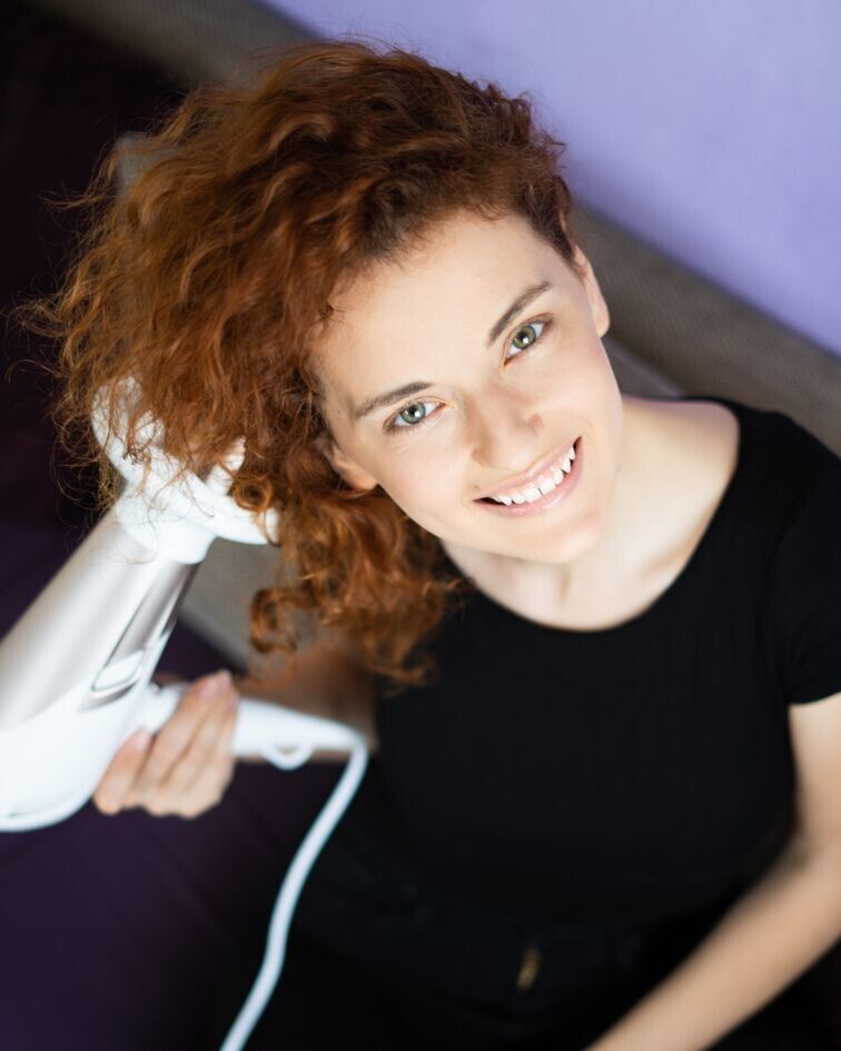 Donna con capelli ricci che usa un asciugacapelli bianco. Vista dall'alto.