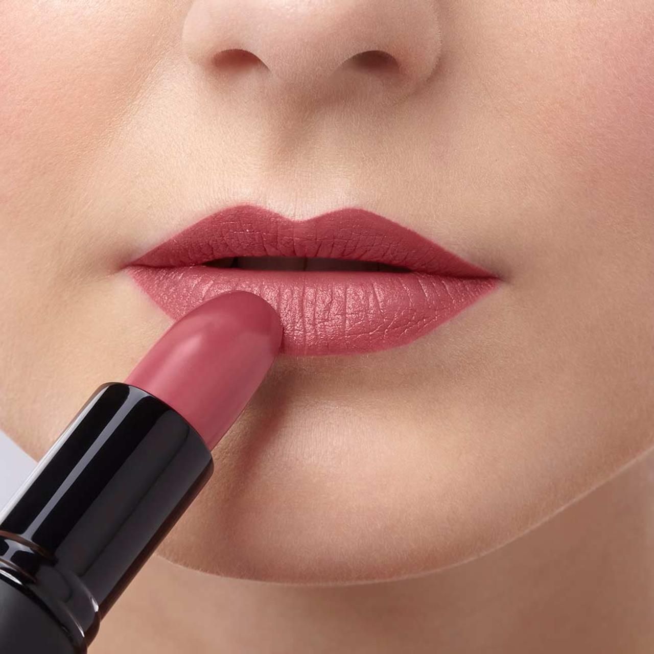 Persona applica rossetto rosa sulle labbra. Portarotolo nero visibile.