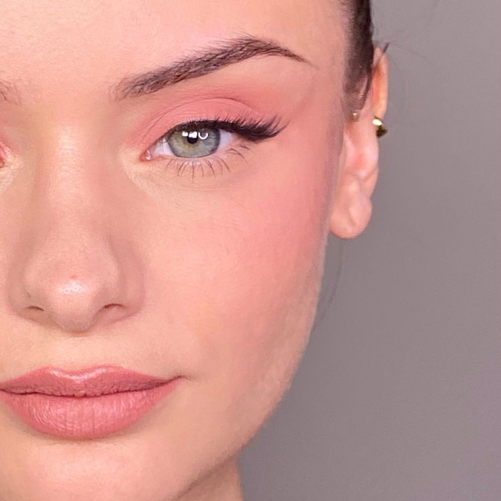 Primo piano di un viso con trucco rosa su occhi e guance. Occhi verdi, orecchino d'oro.