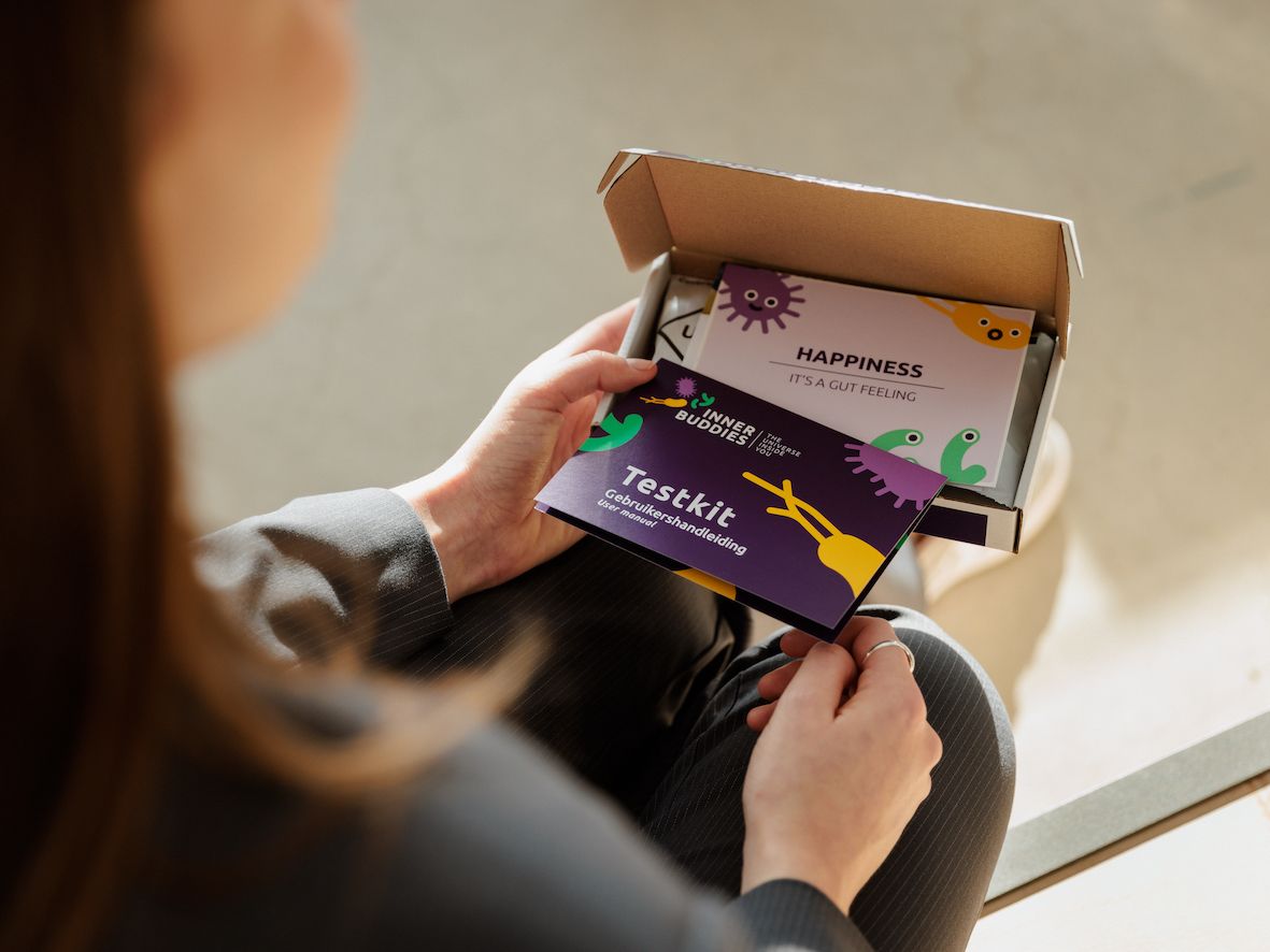 Persona che tiene in mano una carta con la scritta Testkit e un'altra carta con il logo Inner Buddies. Scatola aperta sullo sfondo.