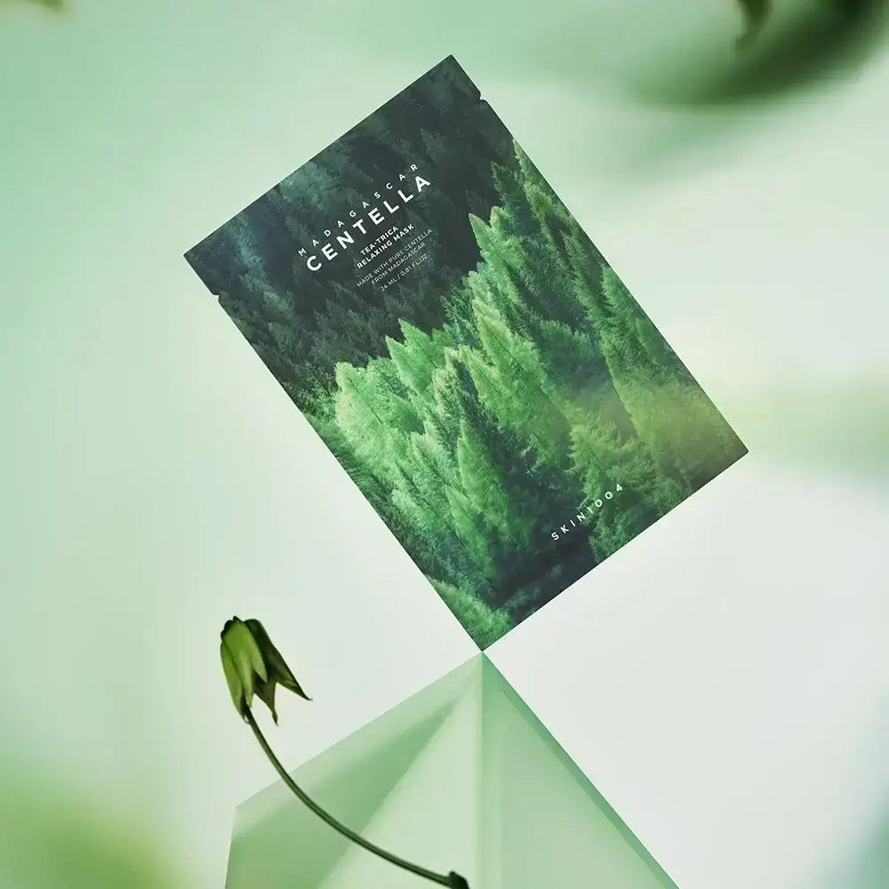 Confezione maschera viso con motivo foresta e scritta MADAGASCAR CENTELLA. Su una superficie di vetro, fiore.