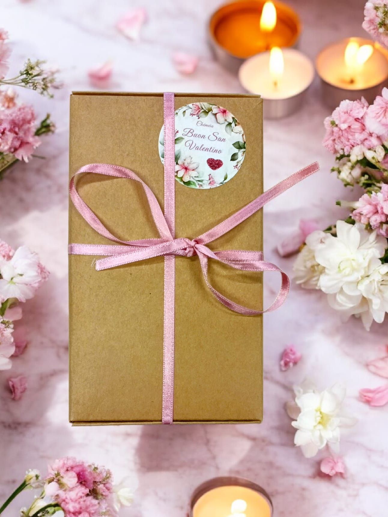 Scatola regalo marrone con fiocco rosa e adesivo. Adesivo con motivo floreale e testo.