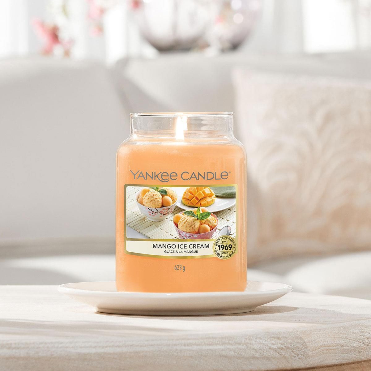 Candela in vaso su piatto bianco. Etichetta con motivo gelato al mango. Marchio Yankee Candle. Scritta: Mango Ice Cream.