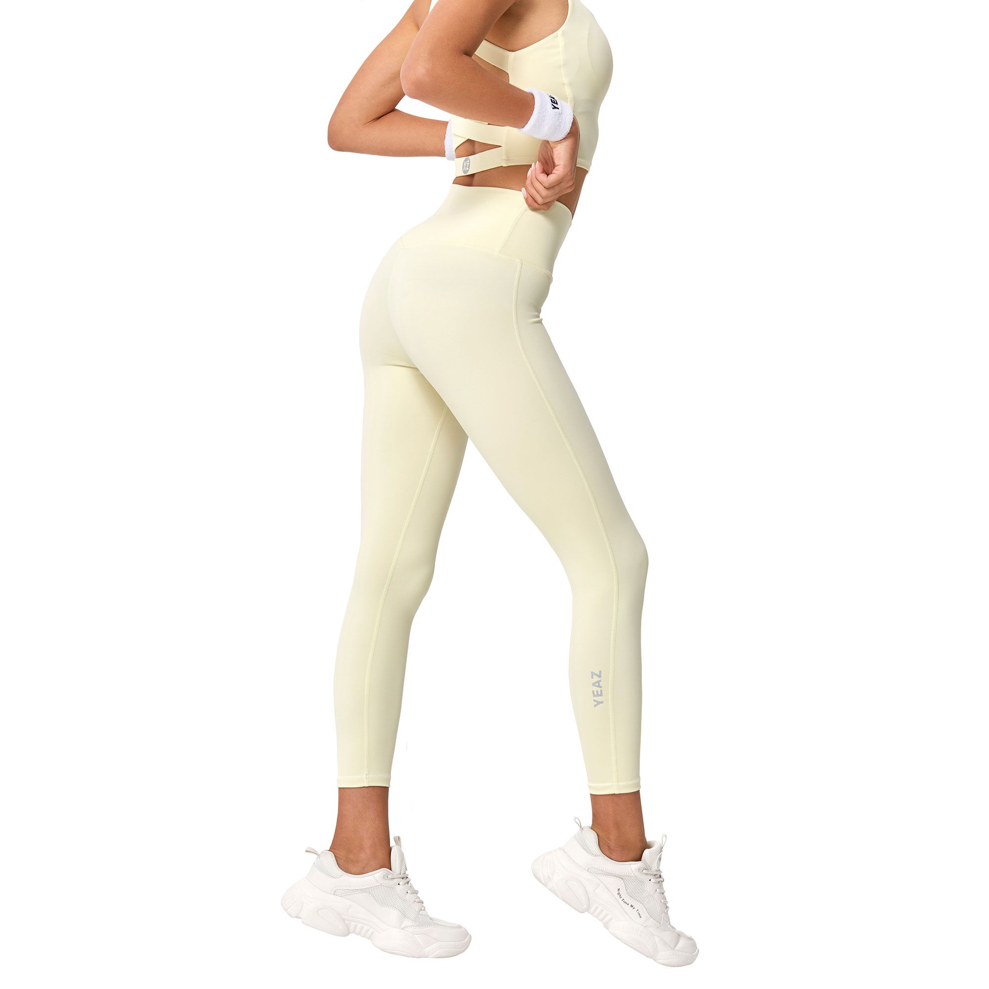 Una donna indossa leggings giallo pallido e un reggiseno sportivo abbinato, con scarpe da ginnastica bianche.