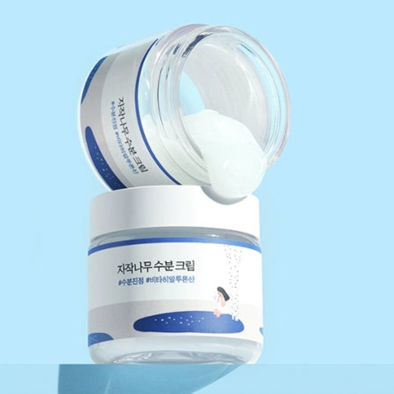Due vasetti di crema. Un vasetto aperto, crema visibile. Etichette blu con testo.
