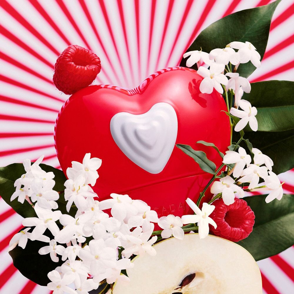 Flacone a forma di cuore rosso con cuore bianco. Decorato con fiori di gelsomino, lamponi e fetta di pera. Sfondo a strisce rosse.