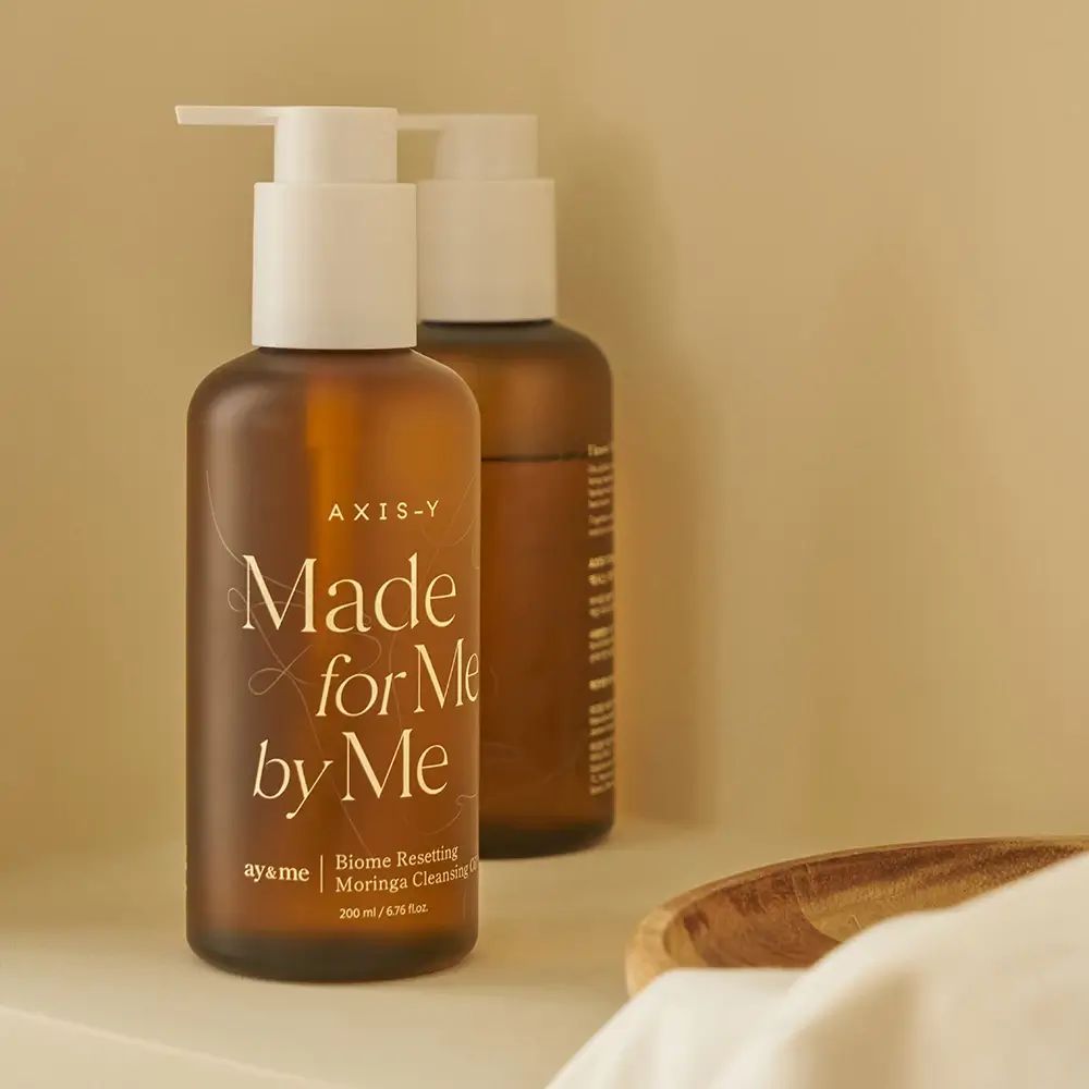 Due flaconi marroni con erogatore bianco. Scritta: AXIS-Y, Made for Me by Me, Biome Resetting Moringa Cleansing Oil.