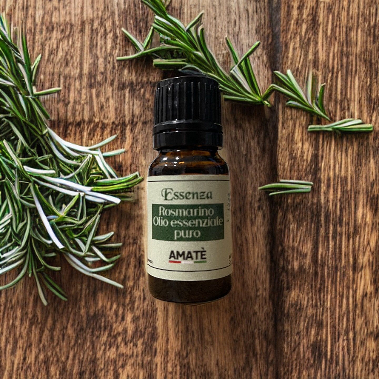 Flacone di vetro marrone con tappo nero, circondato da rametti di rosmarino. Etichetta: Essenza Rosmarino Olio essenziale puro. Marchio: AMATÈ.