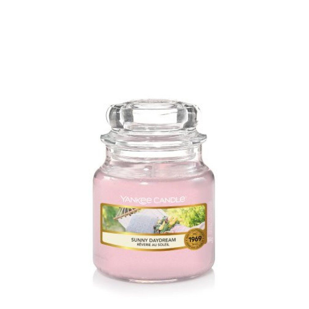 Piccola candela profumata in barattolo di vetro, cera rosa, etichetta con testo e immagine, coperchio. Scritta: Yankee Candle, Sunny Daydream, 1969.