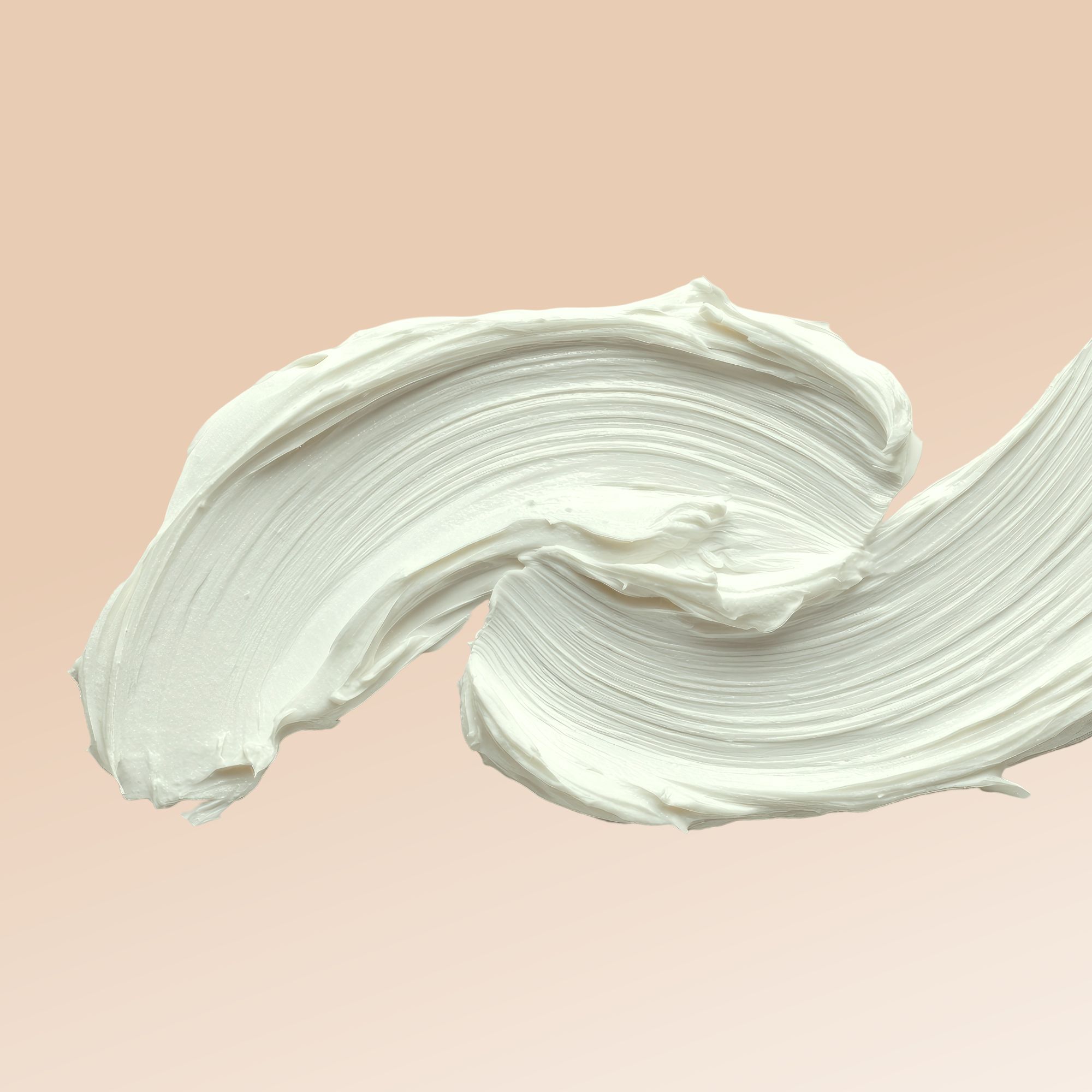 Primo piano di una striscia di crema bianca che si arriccia su uno sfondo marrone chiaro.
