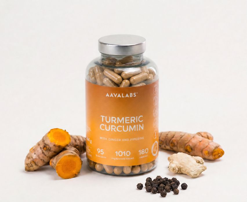 Flacone di capsule di curcuma circondato da radici di curcuma, zenzero e grani di pepe.