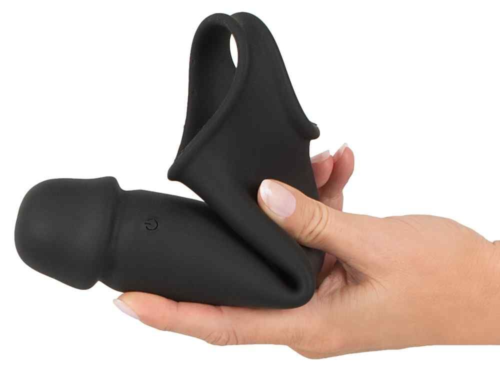 Rivestimento per pene nero con anello per le palle, tenuto in una mano. Il rivestimento è parzialmente piegato. L'anello per le palle è visibile.