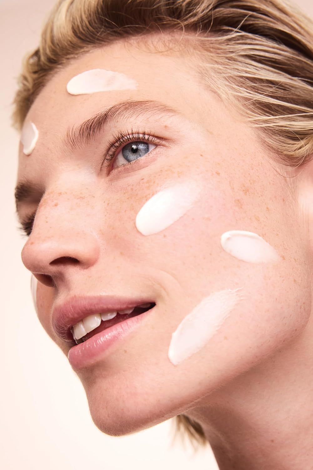 Viso di donna con punti di crema sulla pelle. Sorride.