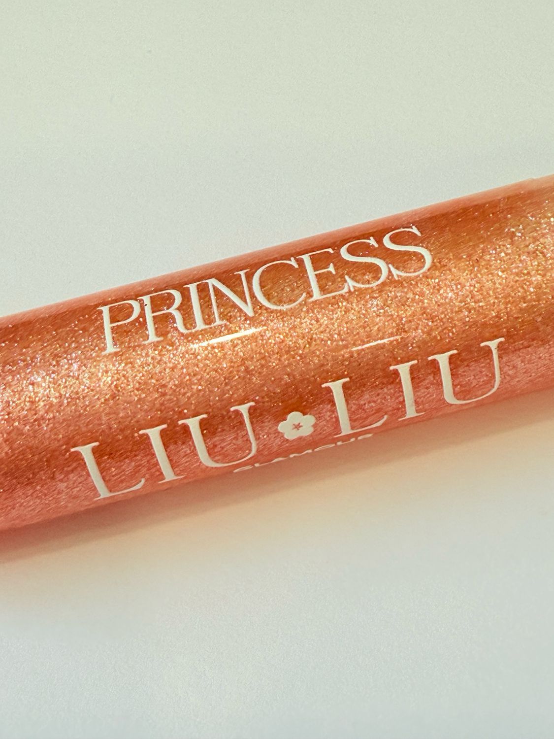 Primo piano di un lucidalabbra rosa glitterato. Scritta: PRINCESS LIU LIU Glamour. Sfondo bianco. Tappo dorato.