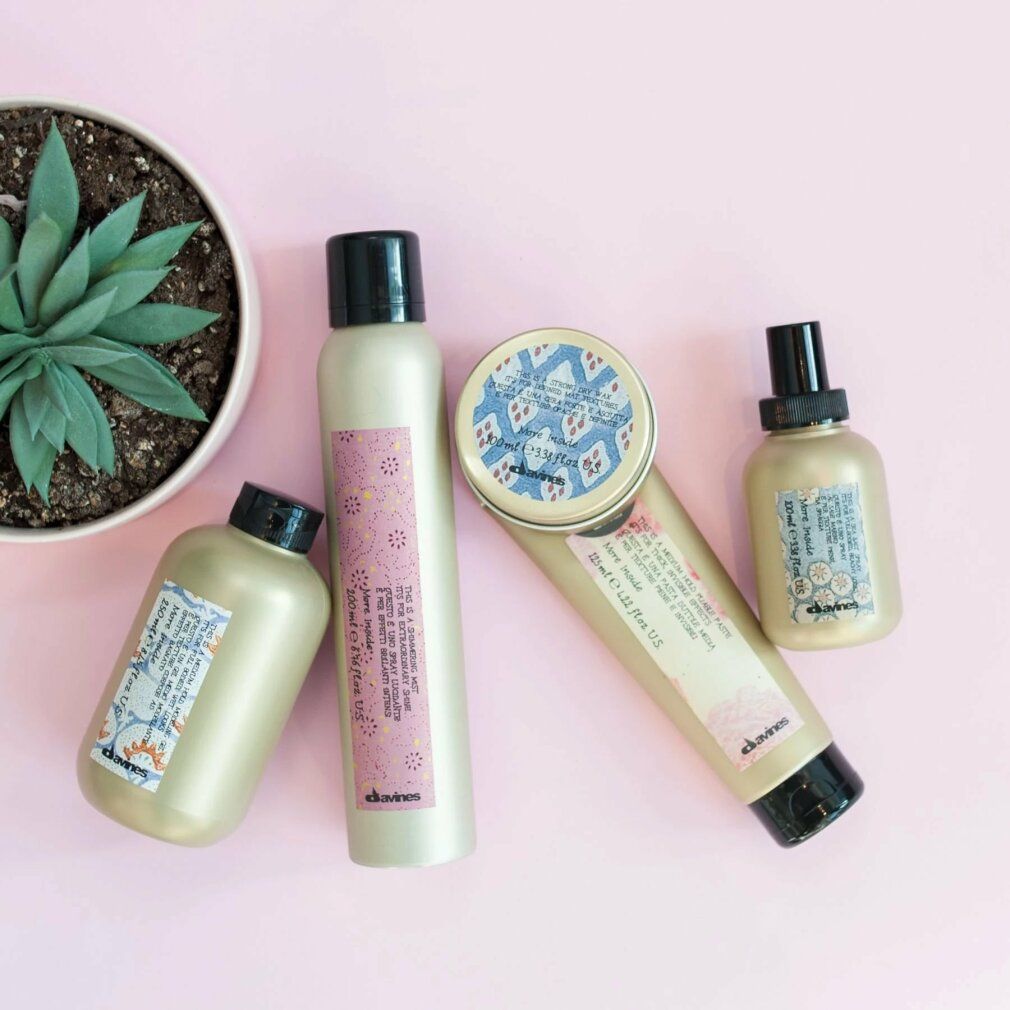 Diversi contenitori con tappi neri ed etichette. Scritta: Davines, 200 ml, testo in inglese. Su sfondo rosa.