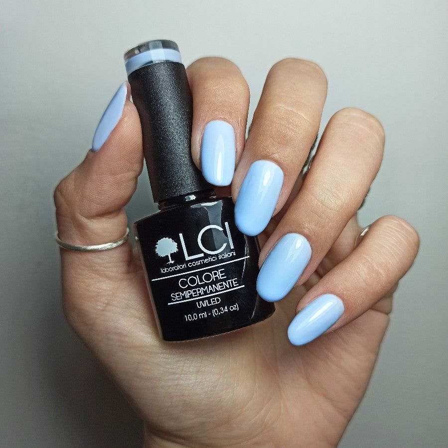 Mano con unghie smaltate e flacone di smalto. Smalto blu chiaro. Flacone nero con etichetta e marchio.