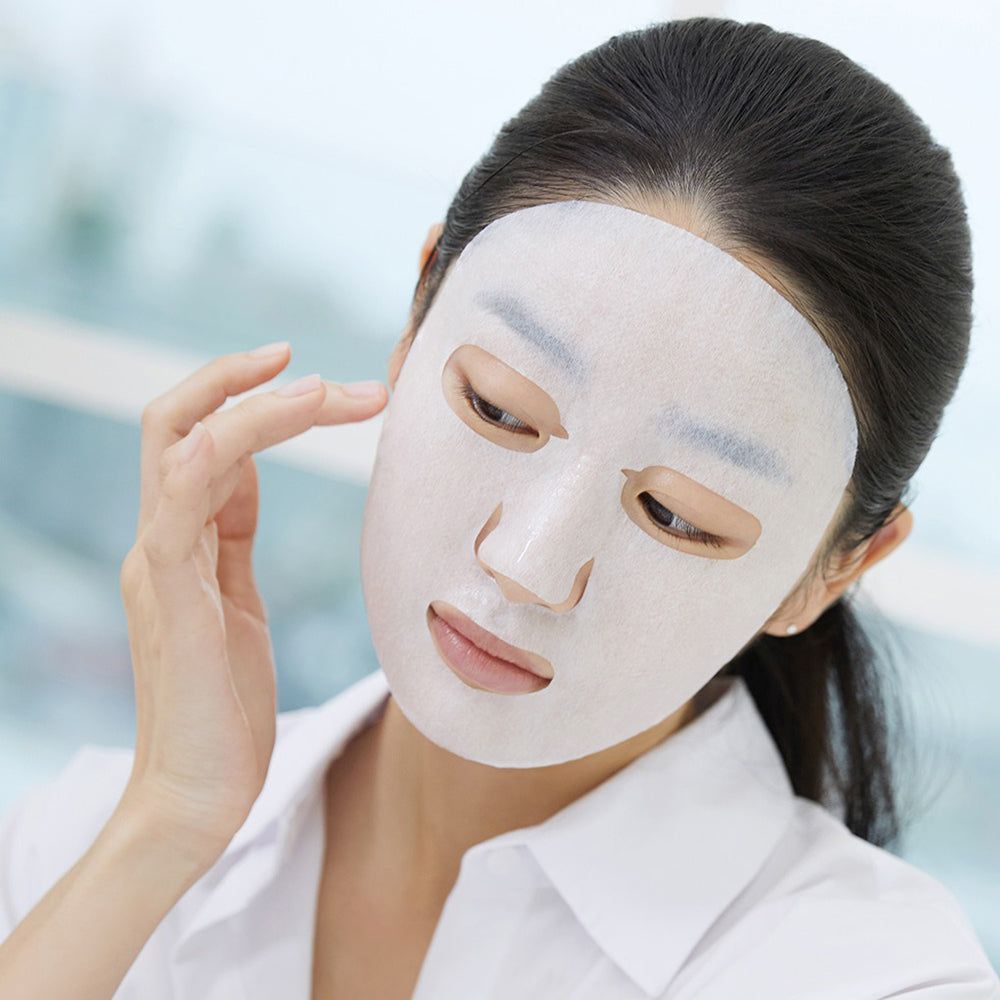 Una donna con una maschera facciale bianca, che si tocca delicatamente il viso.