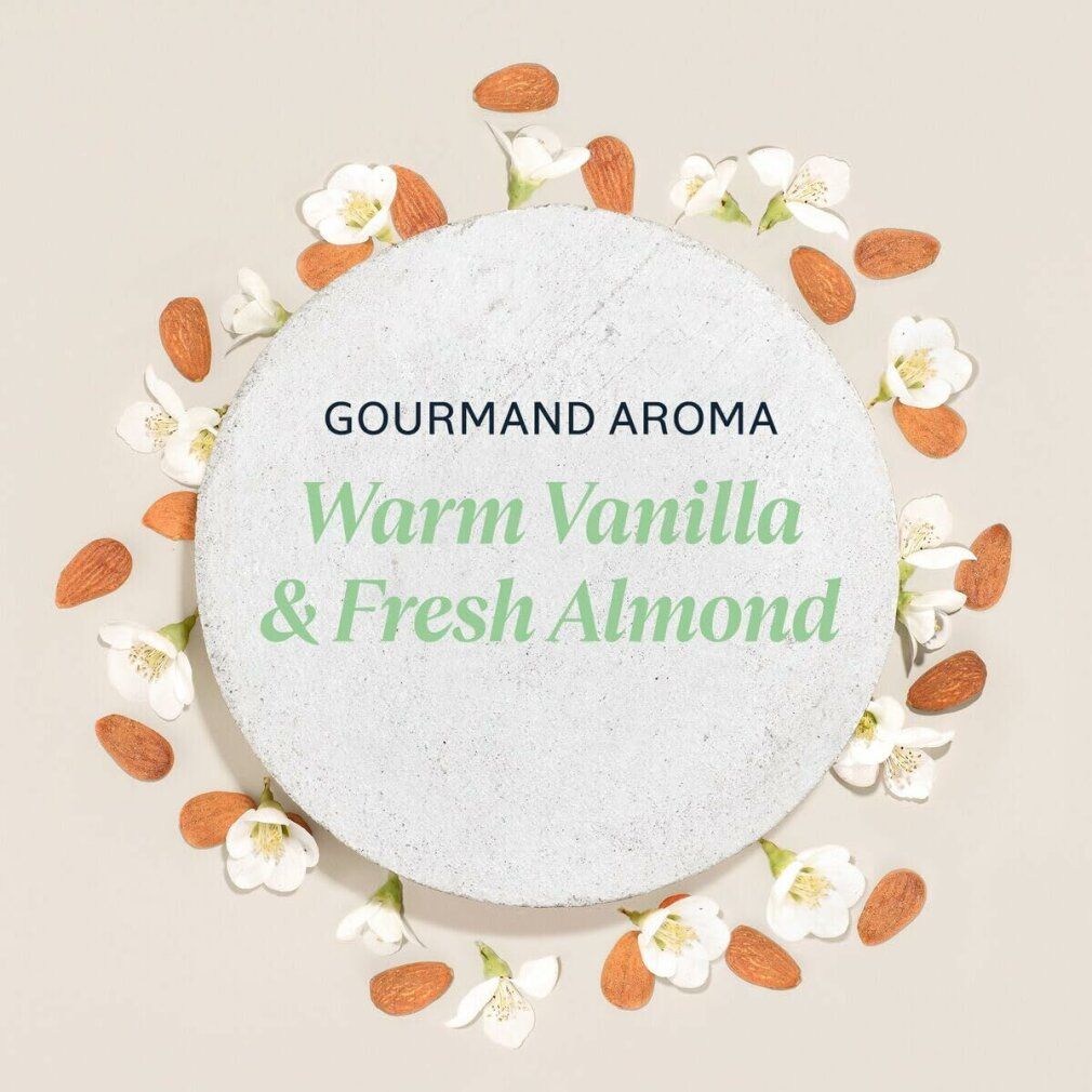 Pietra rotonda con testo: Gourmand Aroma, Warm Vanilla & Fresh Almond. Circondata da mandorle e fiori.