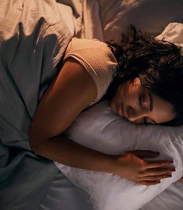 Una donna dorme su un cuscino sotto una coperta. Capelli scuri, occhi chiusi. Ambiente camera da letto.