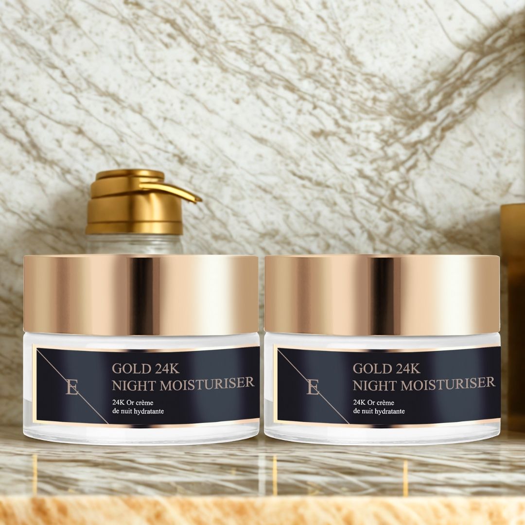 Due vasetti con coperchi dorati. Etichette nere con testo: GOLD 24K NIGHT MOISTURISER. Logo "E". Su ripiano.