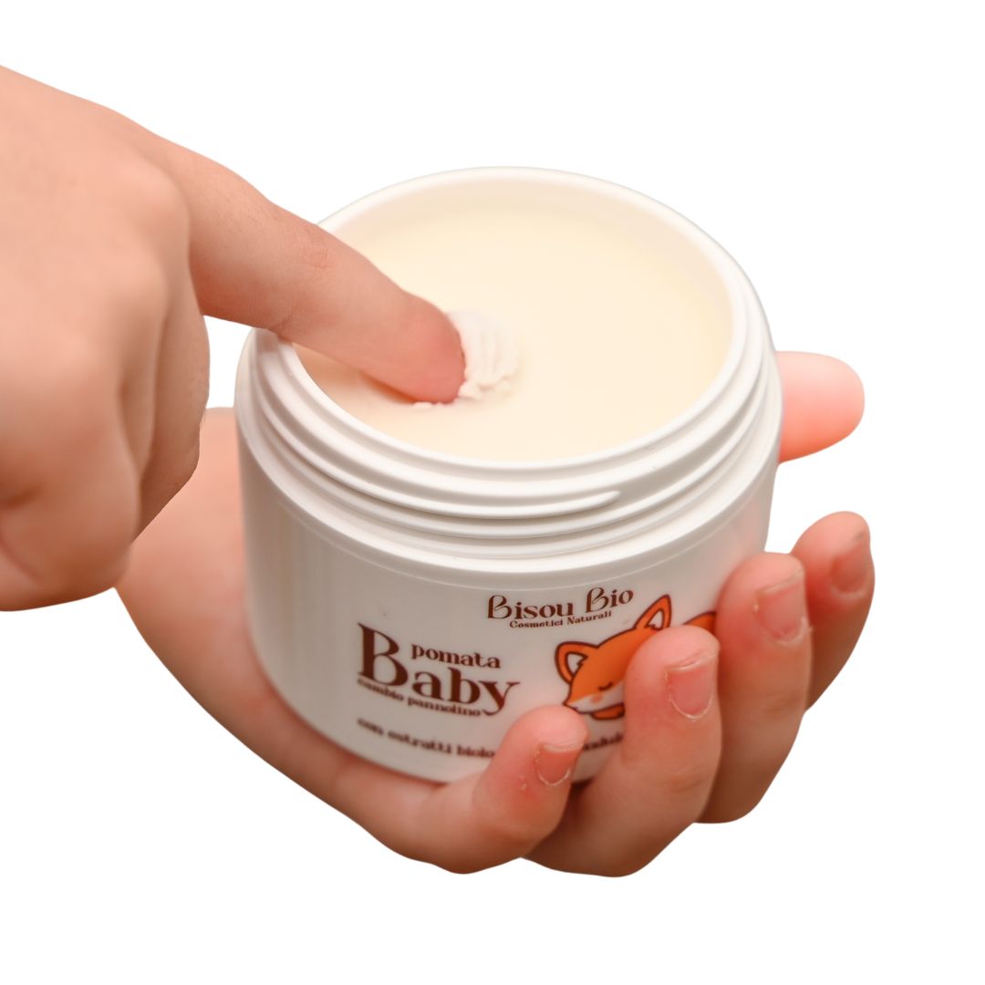 Vasetto bianco con crema, tenuto in mano. Scritta 'Bisou Bio Pomata Baby'. Un dito tocca la crema.
