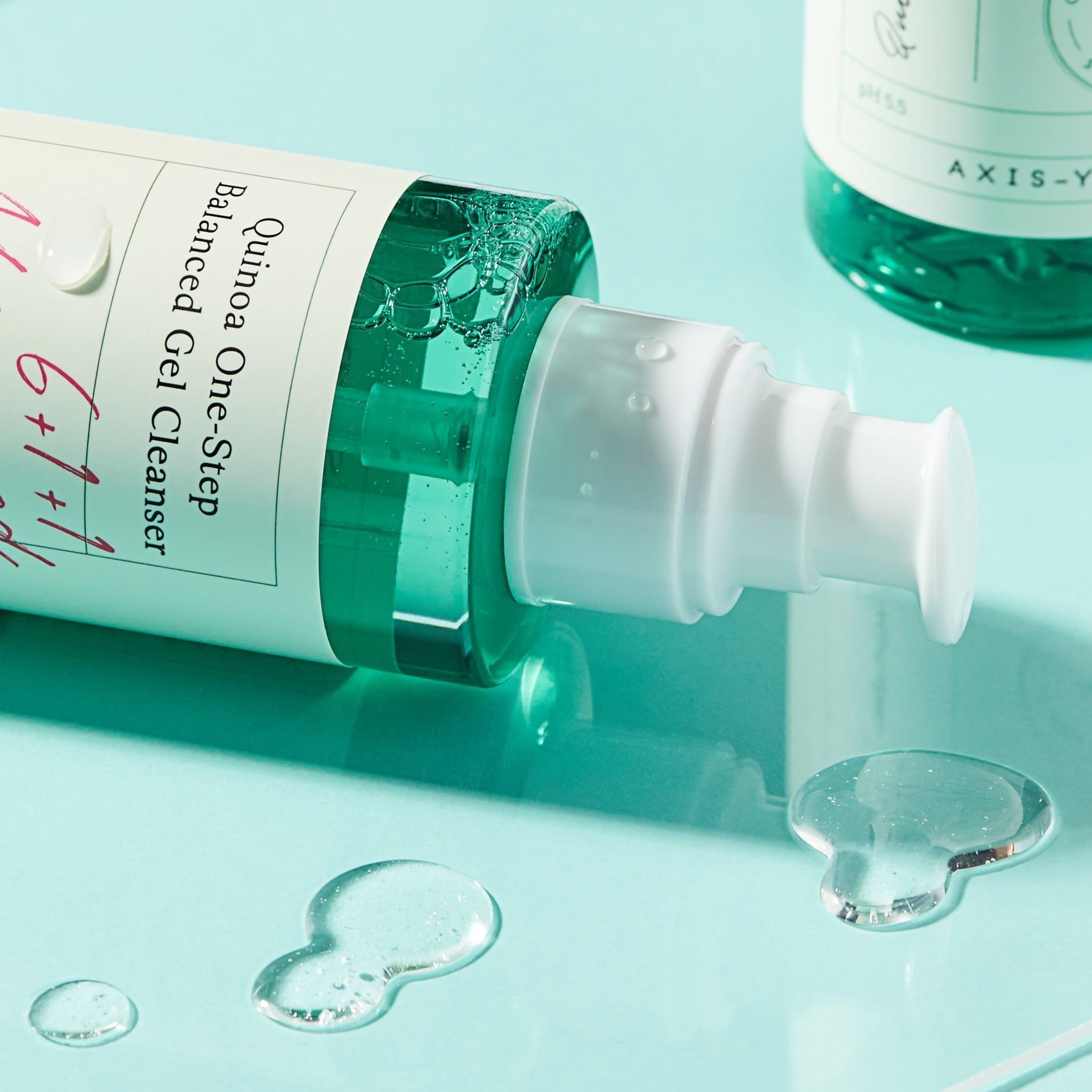 Primo piano del collo della bottiglia. Scritta: Quinoa One-Step Balanced Gel Cleanser, 6+1+1 Advanced Formula. Gocce d'acqua e liquido.