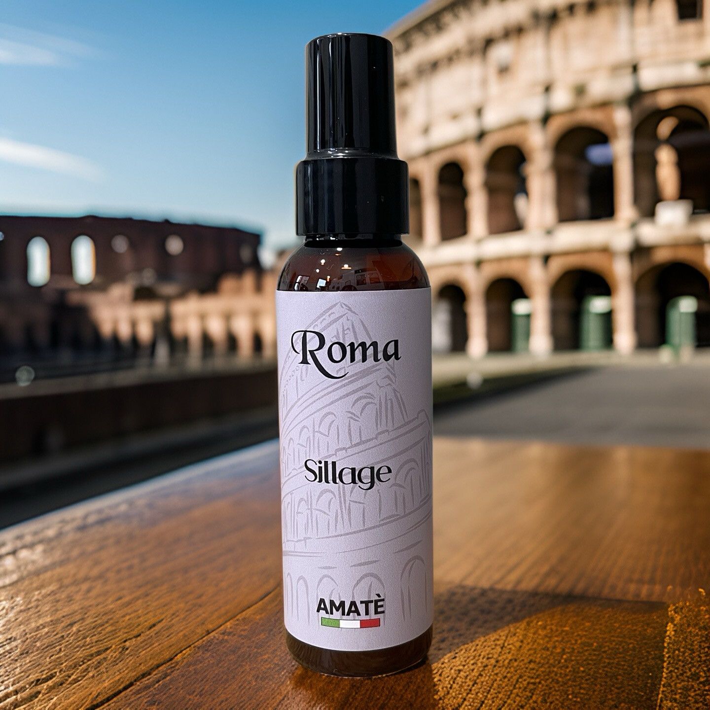 Flacone marrone con vaporizzatore nero su legno, davanti al Colosseo. Scritta "Roma Sillage" e "AMATÈ".