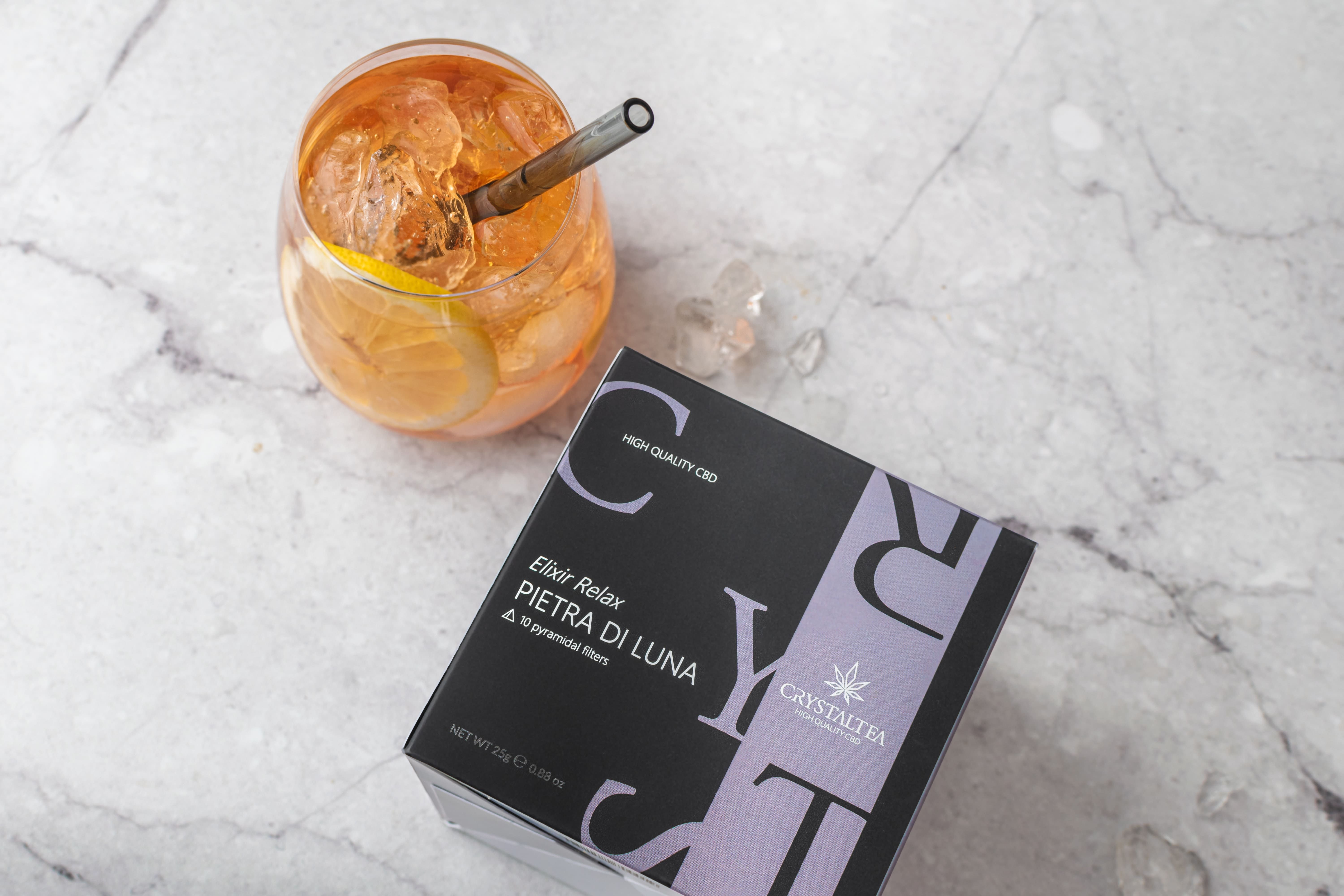 Bicchiere con bevanda, cubetti di ghiaccio e cannuccia. Accanto, scatola con nome e logo del prodotto.