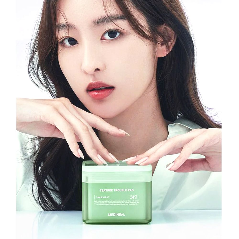 Donna che tiene una scatola verde. Scritta: TEA TREE TROUBLE PAD. Marchio: MEDIHEAL. Donna truccata.