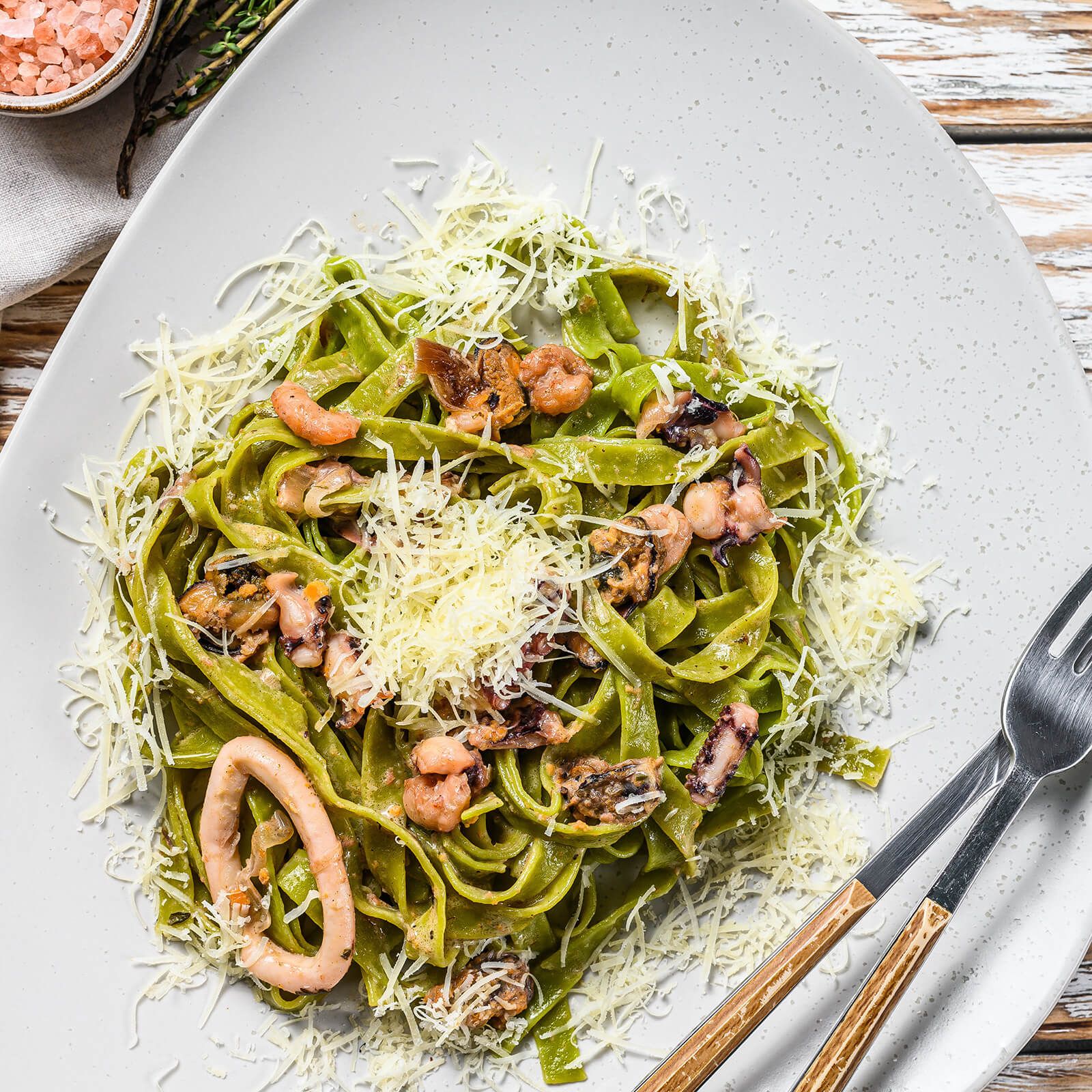 Piatto di tagliatelle verdi, frutti di mare e parmigiano. Con forchette.